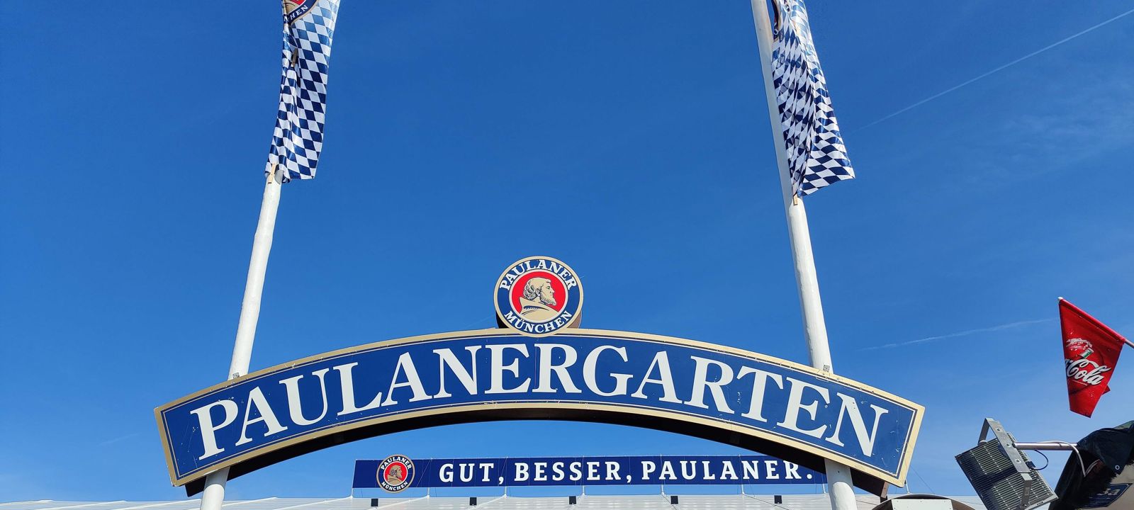 The Paulanergarten arch at Oktoberfest under a blue sky with Bavarian flags