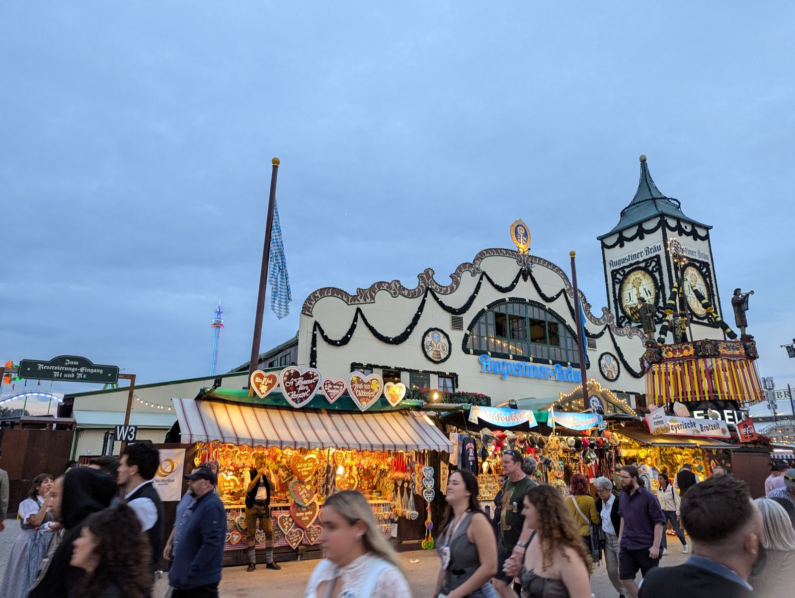 Augustiner-Festhalle facade and clock tower at dusk with a gingerbread-heart stall in front