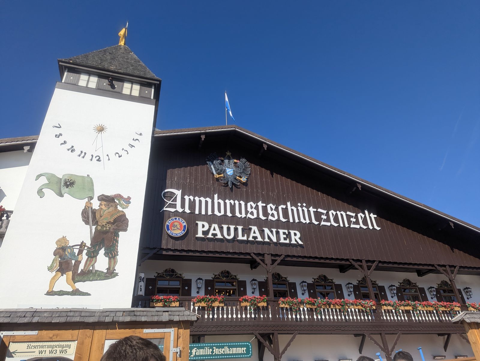 Armbrustschützenzelt facade with Paulaner signage and its painted tower under a blue sky