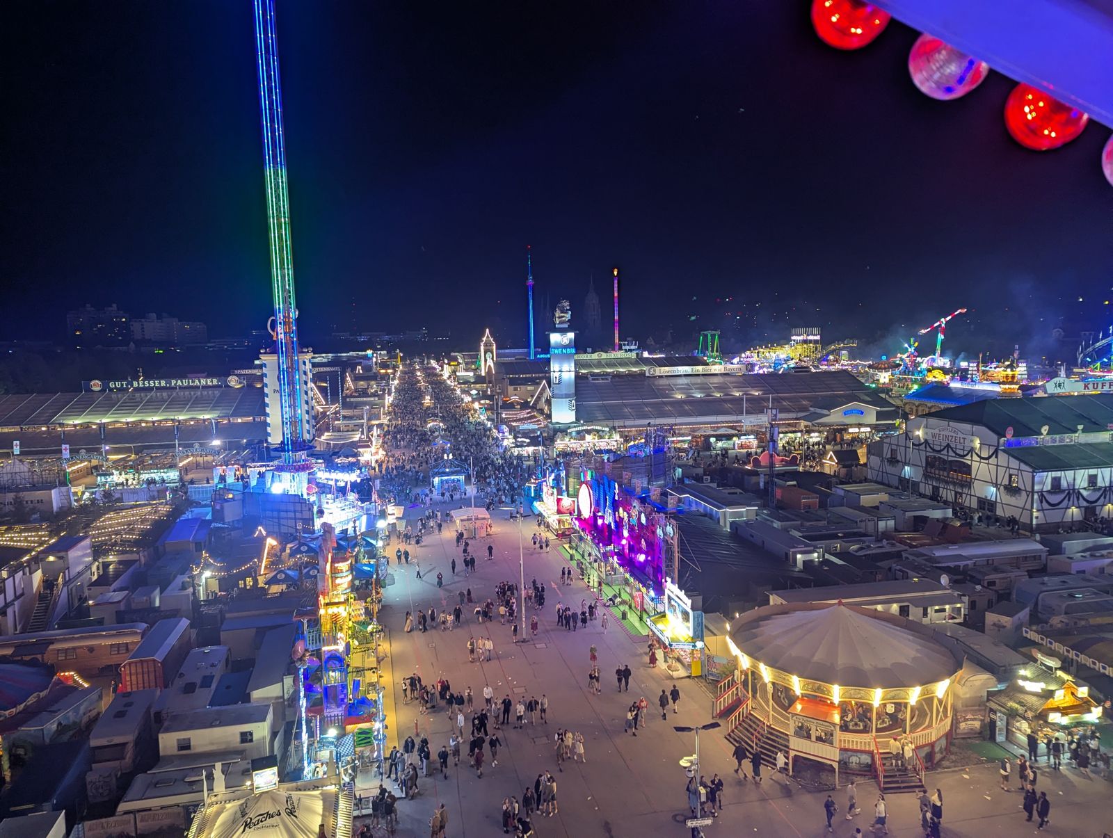 Night aerial view of the lit Oktoberfest grounds and drop tower from the Ferris wheel
