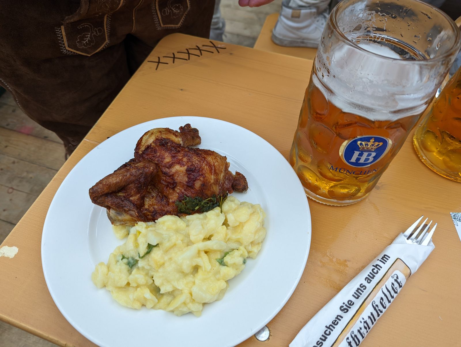 Half a roast chicken with potato salad next to a Hofbräu Maß